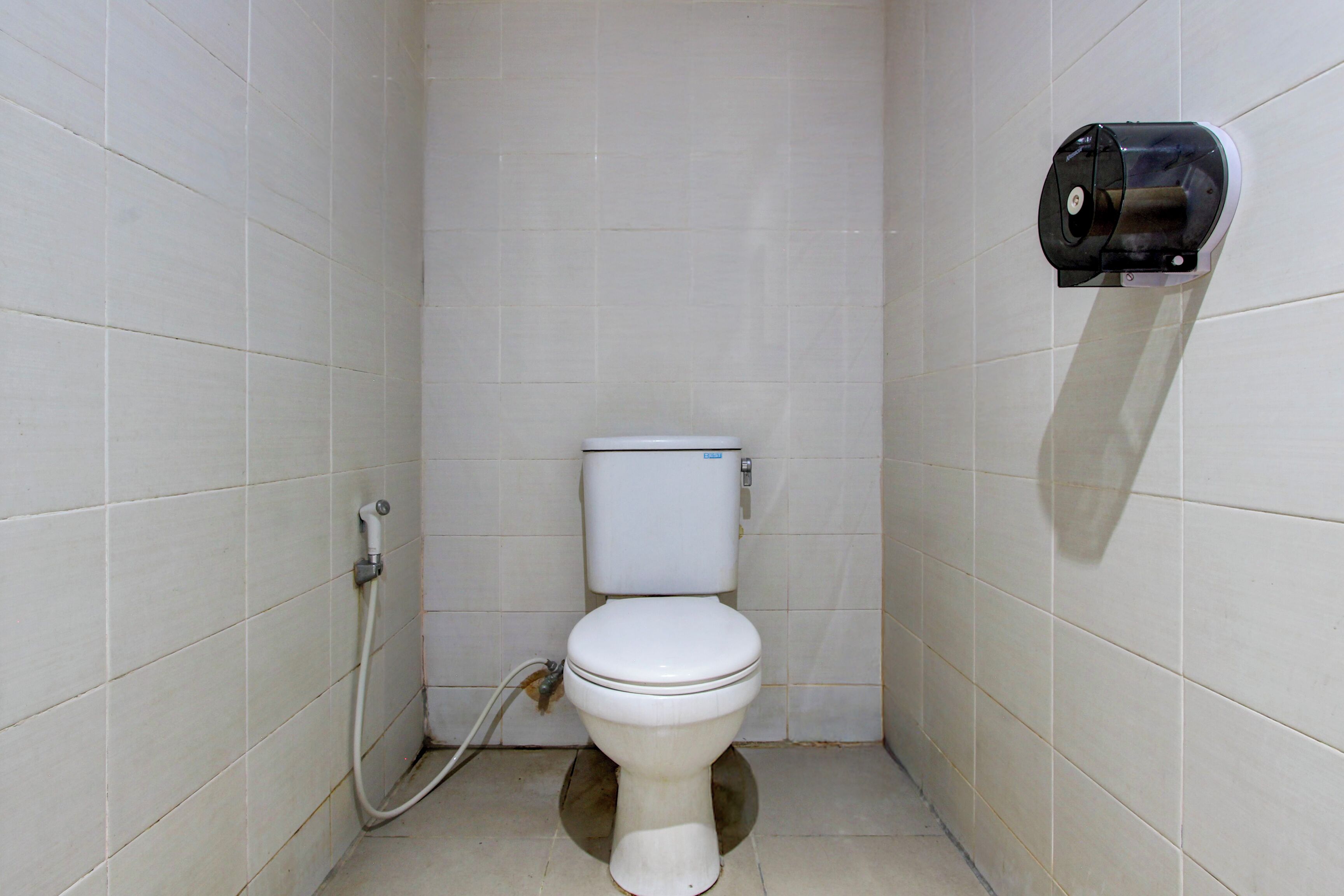 A small, white-tiled bathroom with a toilet, a hand dryer, and a visible water pipe.