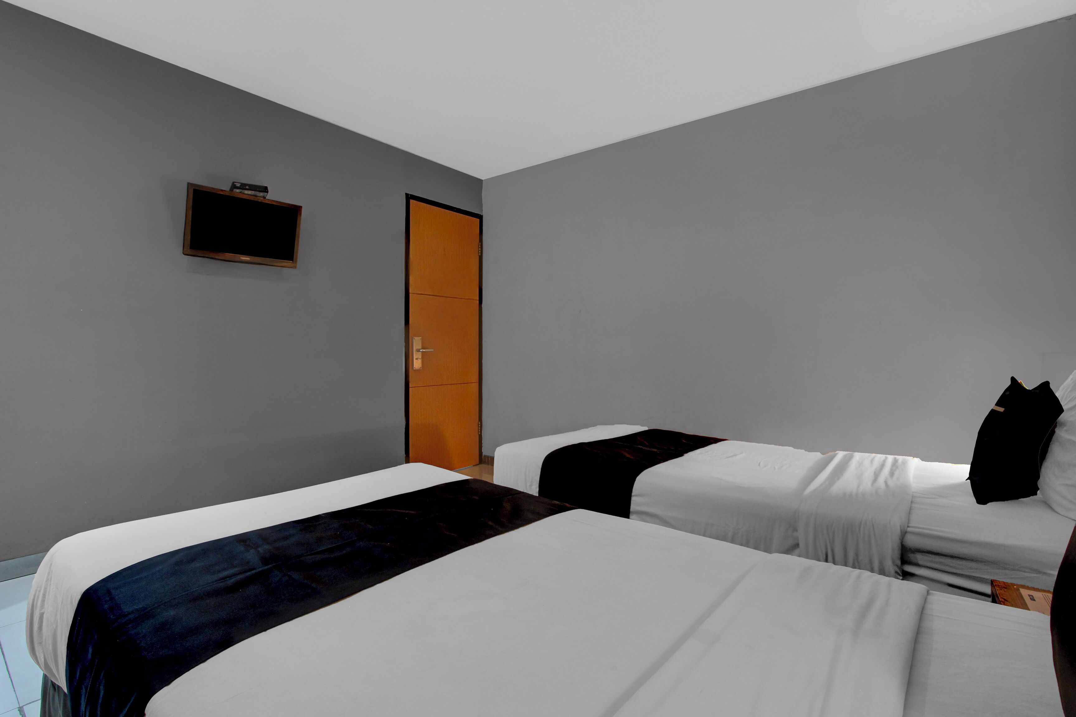 Habitación de hotel con dos camas, un televisor montado en la pared y una puerta.