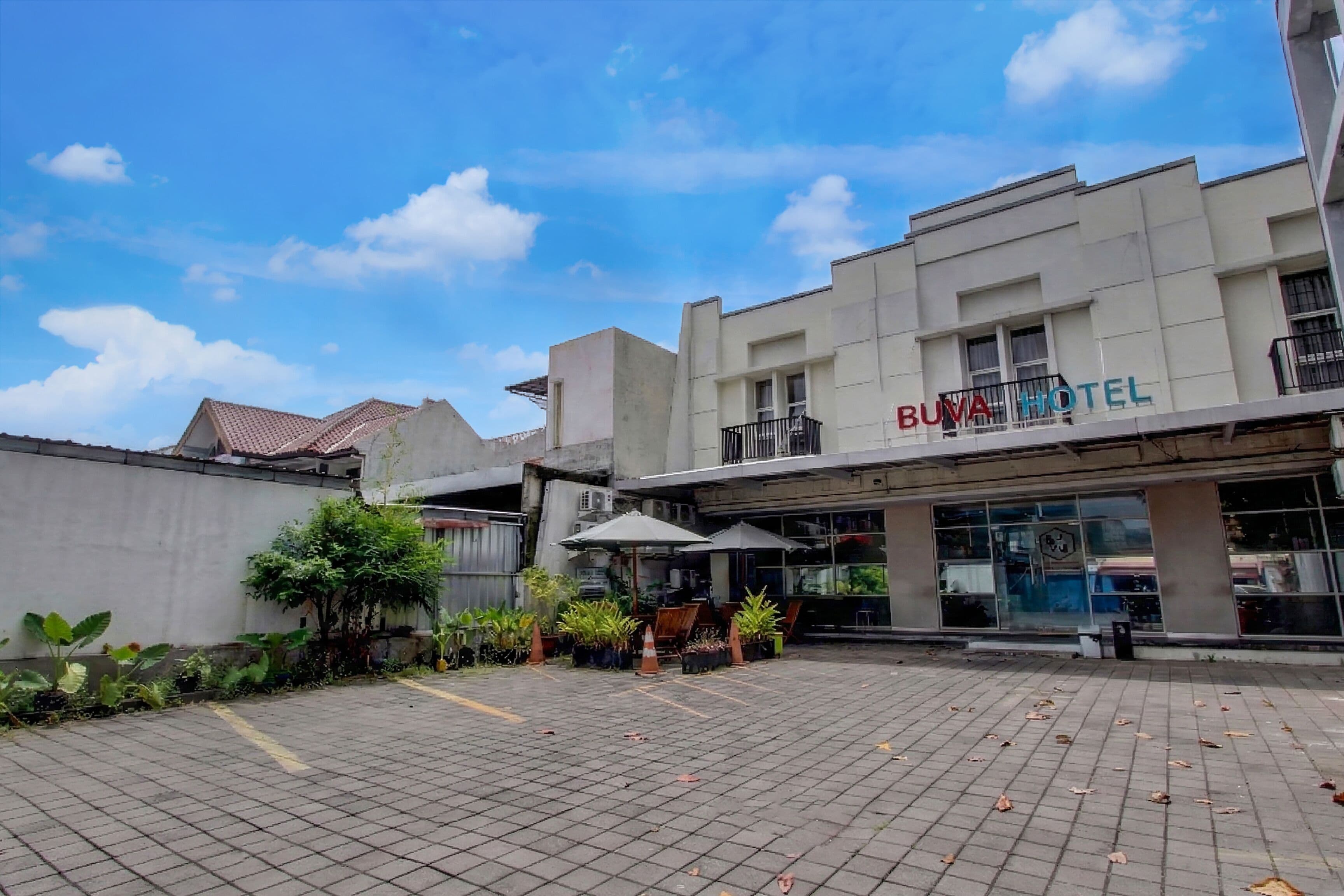 A hotel with a tiled courtyard, outdoor seating, and a sign reading 'BUVA HOTEL'.