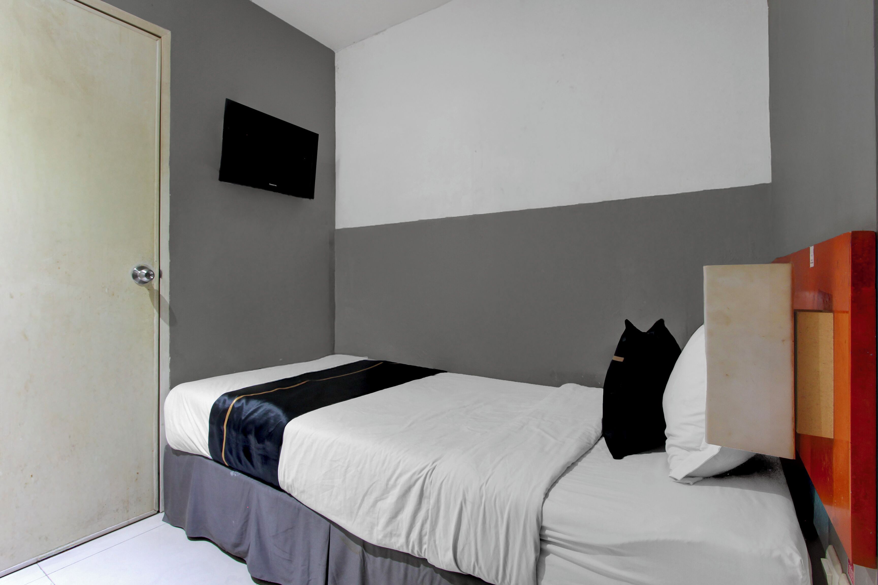 A bedroom with a bed, a television mounted on the wall, and a door.