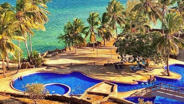 A resort pool area with multiple swimming pools, palm trees, and a view of the ocean. - Duplex Ocean View 1bedroom Apartment D10 ,Top Floor (Mombasa)