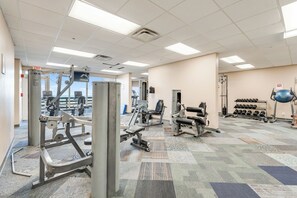 Ein Fitnessraum mit diversen Trainingsgeräten, einem gemusterten Teppich und Blick ins Freie.