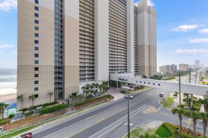 Ein Hochhaus-Hotel mit mehreren Etagen, einer Fußgängerbrücke und einer Straße mit Palmen und einem Strand im Hintergrund.