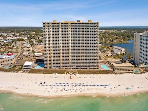Ein Hochhaus-Hotel mit mehreren Etagen, ein Strand im Vordergrund und ein Gewässer im Hintergrund.