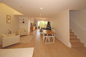 A spacious living area with a wooden dining table, a sofa, and a staircase. - Spacious Marcoola seaside 3-bedroom apartment (Marcoola)