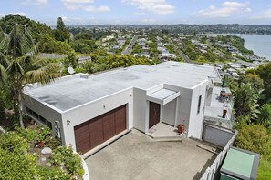 A modern building with a flat roof, a garage, and a small patio area. - Clifftop Glasshouse with Sweeping Views (Whangaparāoa)