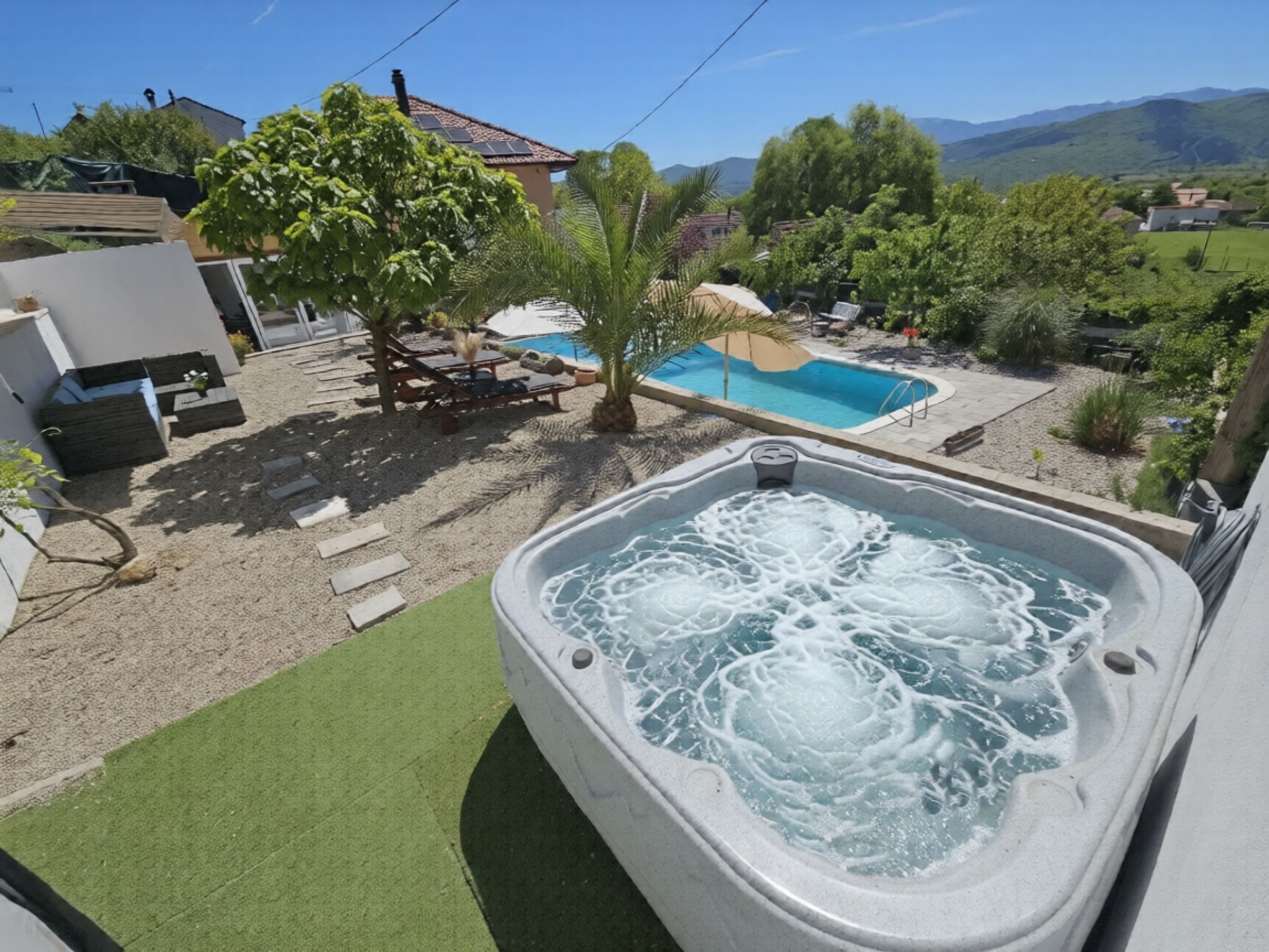 Ein Whirlpool mit Pool im Hintergrund, umgeben von Grünpflanzen und einem klaren Himmel.