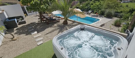 Ein Whirlpool mit Pool im Hintergrund, umgeben von Grünpflanzen und einem klaren Himmel.