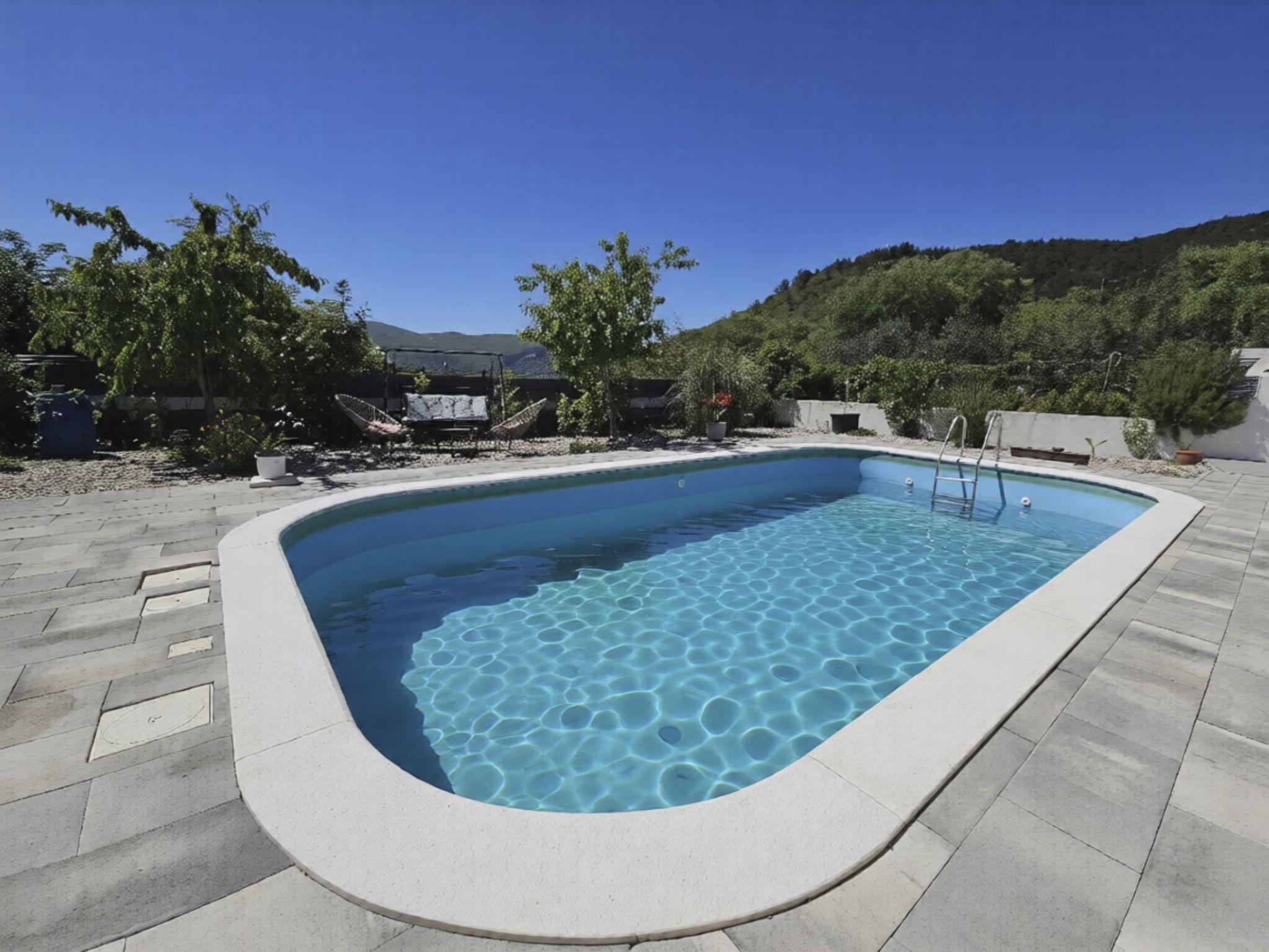 A rectangular swimming pool with a clear blue water surface, surrounded by a paved deck.