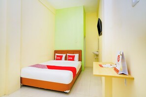 Una habitación de hotel con cama, mesita de noche, espejo y televisión montada en la pared.