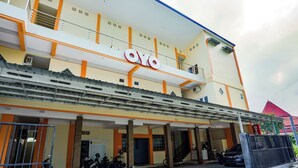 Un edificio con un llamativo letrero 'OYO', un acceso cubierto y un área de estacionamiento con motocicletas y un automóvil.