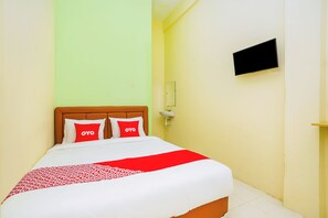 Habitación de hotel con cama, dos almohadas con la palabra 'OYO', una colcha estampada en rojo y blanco, un televisor montado en la pared y un pequeño estante.