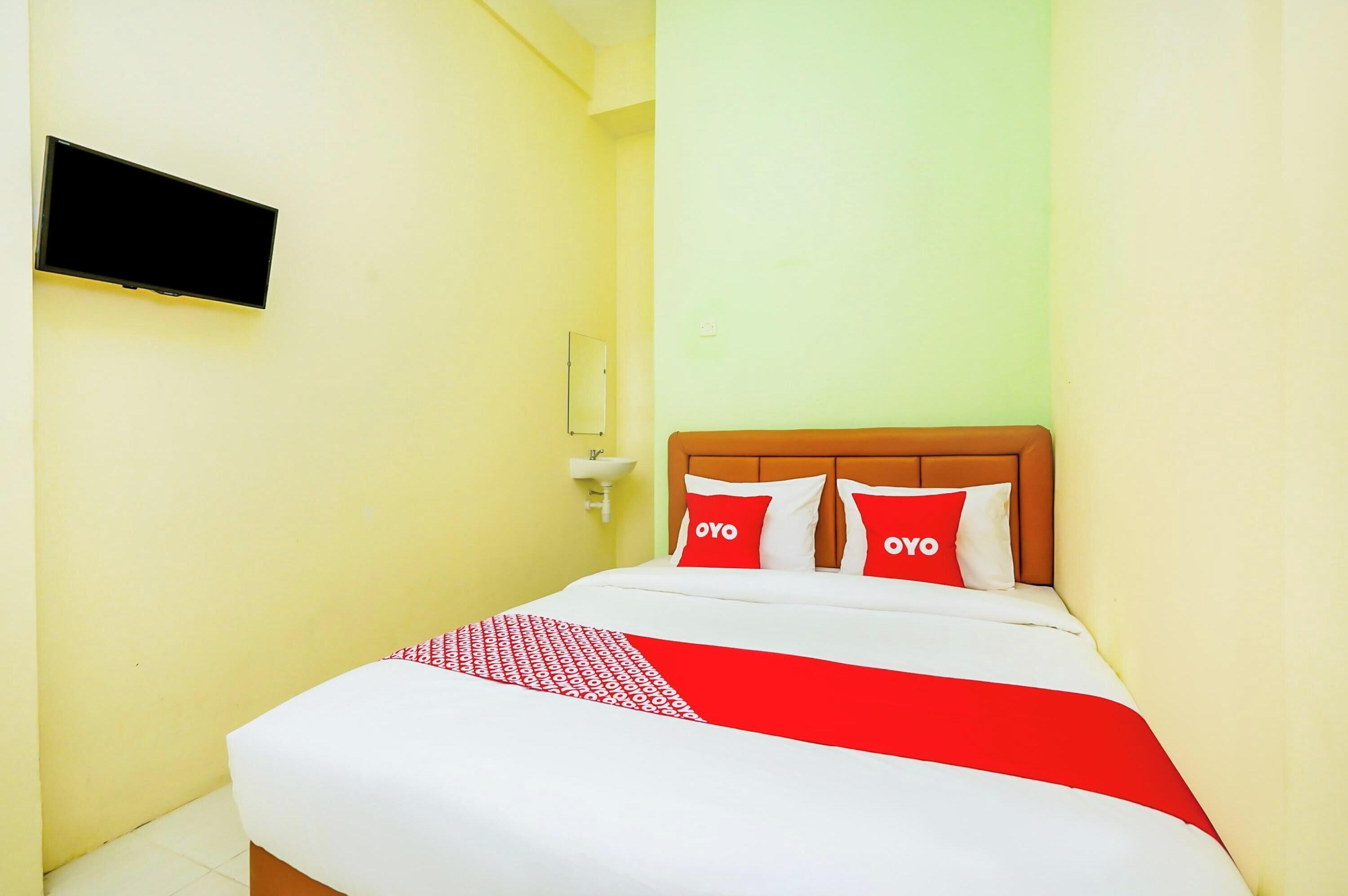 A hotel room with a bed, a TV mounted on the wall, and a small sink.