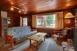 Ein gemütliches Blockhaus-Interieur mit einer Couch, einem Holztisch, einem Ledersessel und einem Kamin aus Stein.