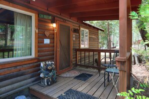 Eine Holzhütte mit Veranda, Geländer, einer Tür mit Herzdeko und einer kleinen Bärenstatue vor den Stufen.