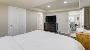 Een slaapkamer met een groot bed, een dressoir, een televisie en een deur naar een andere kamer.