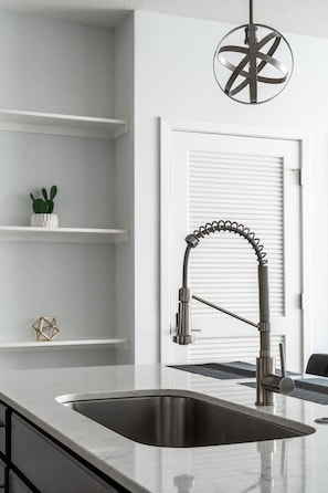 A modern kitchen with a stainless steel sink, a unique faucet, and a pendant light. - Affordable 2-bedroom Fishers Pool View (Fishers)