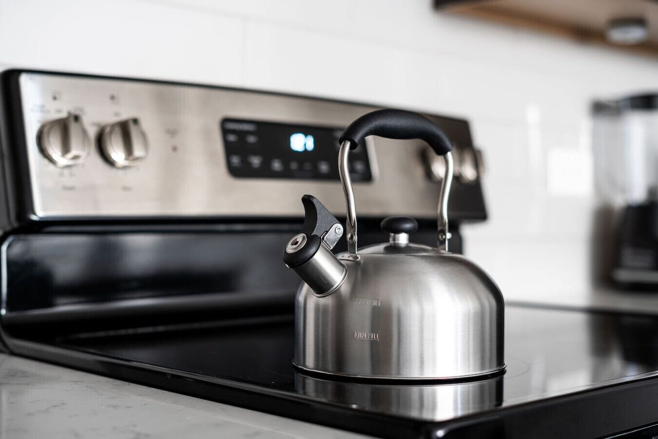 A stainless steel kettle on a black stovetop with a digital control panel in the background.