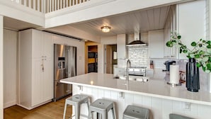A modern kitchen with white cabinetry, stainless steel appliances, and a central island with stools. - 1896 S Fletcher Ave (Fernandina Beach)