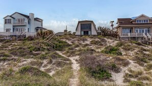A beachfront property with a sandy path leading to a house with a large window and a balcony. - 1896 S Fletcher Ave (Fernandina Beach)