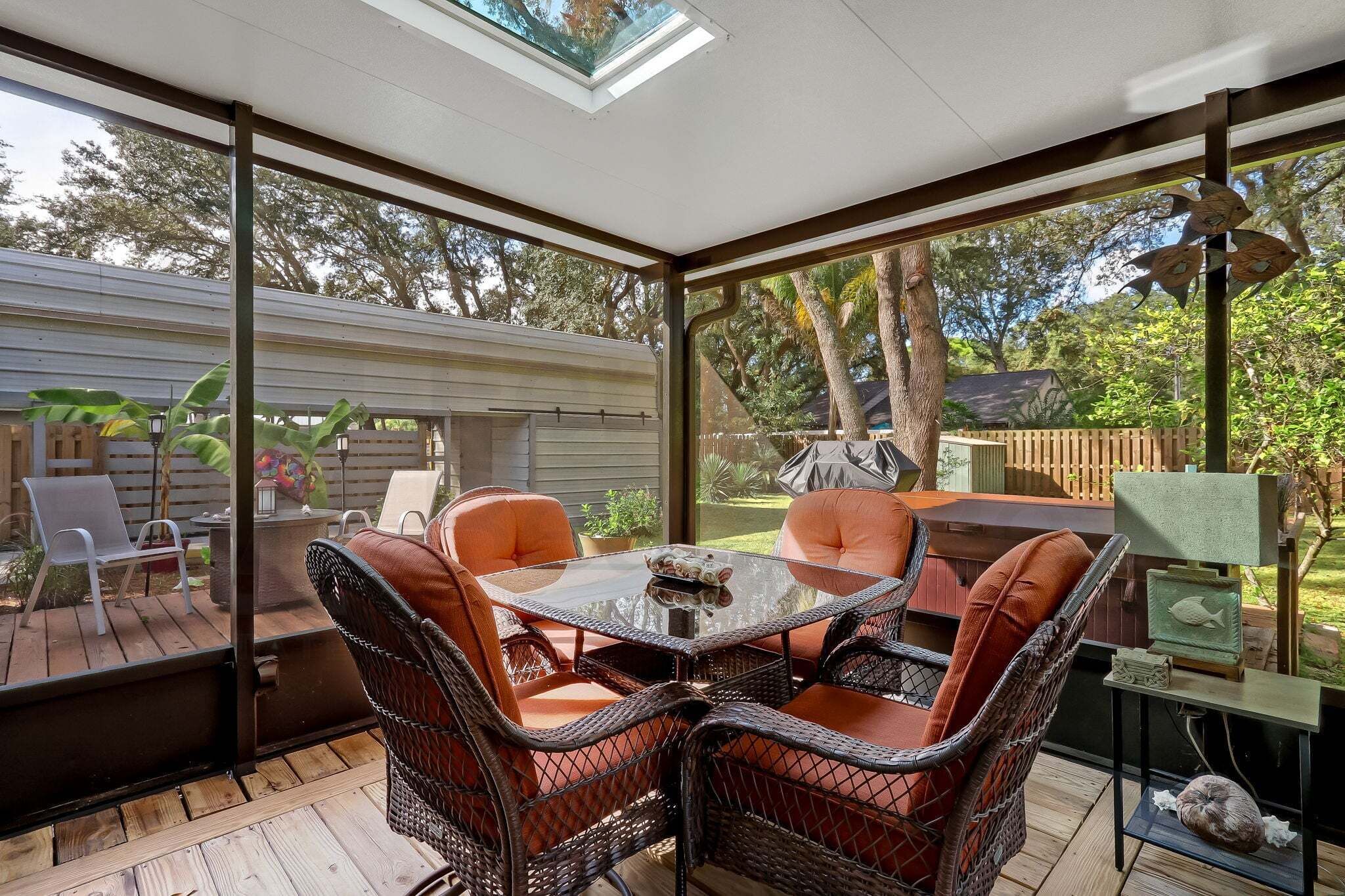 Un patio techado con sillas de mimbre, una mesa de vidrio y vista al jardín trasero.