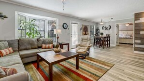 A living room with a sofa, coffee table, and a dining area with chairs and a table. - 2113 Talbot Ct (Fernandina Beach)