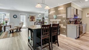 A modern kitchen with a central island, wooden accents, and a dining area with chairs. - 2113 Talbot Ct (Fernandina Beach)