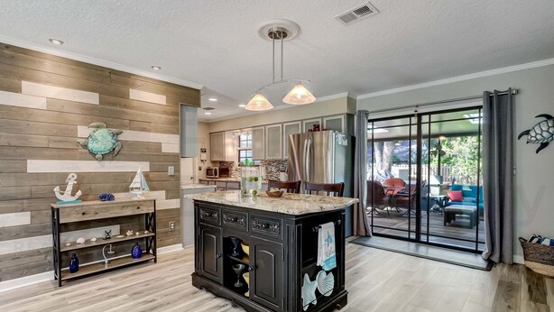 A modern kitchen with a central island, wooden wall paneling, and a view to a patio area. - 2113 Talbot Ct (Fernandina Beach)