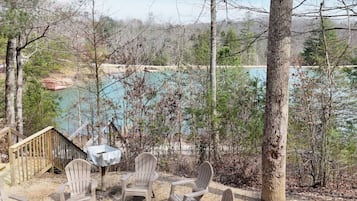 A deck with Adirondack chairs overlooking a lake, surrounded by trees.