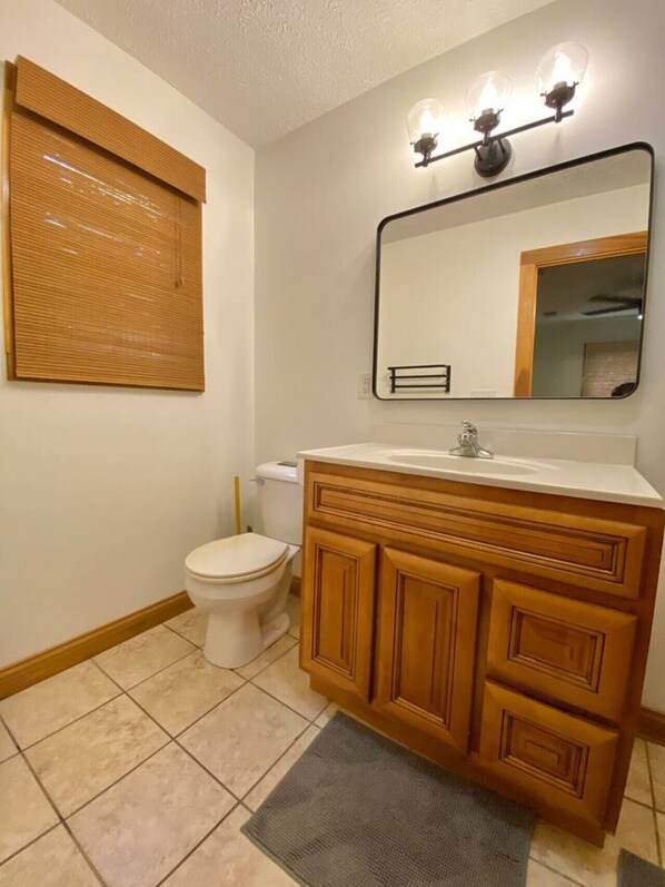 A bathroom with a wooden vanity, a toilet, a wall-mounted mirror, and a light fixture above the mirror. - 14 Guest, 7 Bed, 4 BR, Lakefront Cabin w/ Hot Tub (Rogers)