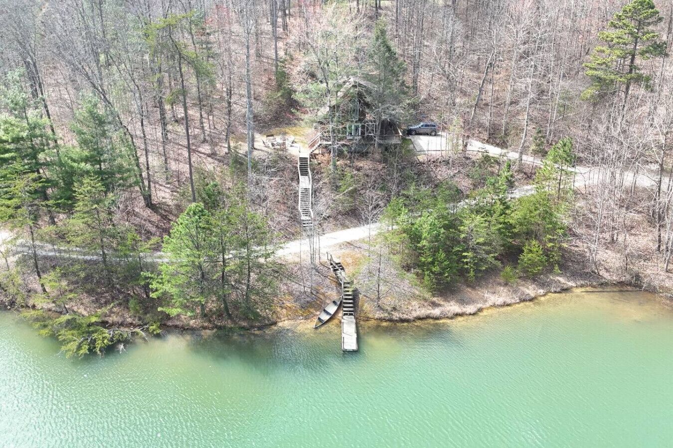 Een chalet omringd door een bos, een steiger die in een meer uitloopt, en een trap naar het chalet.