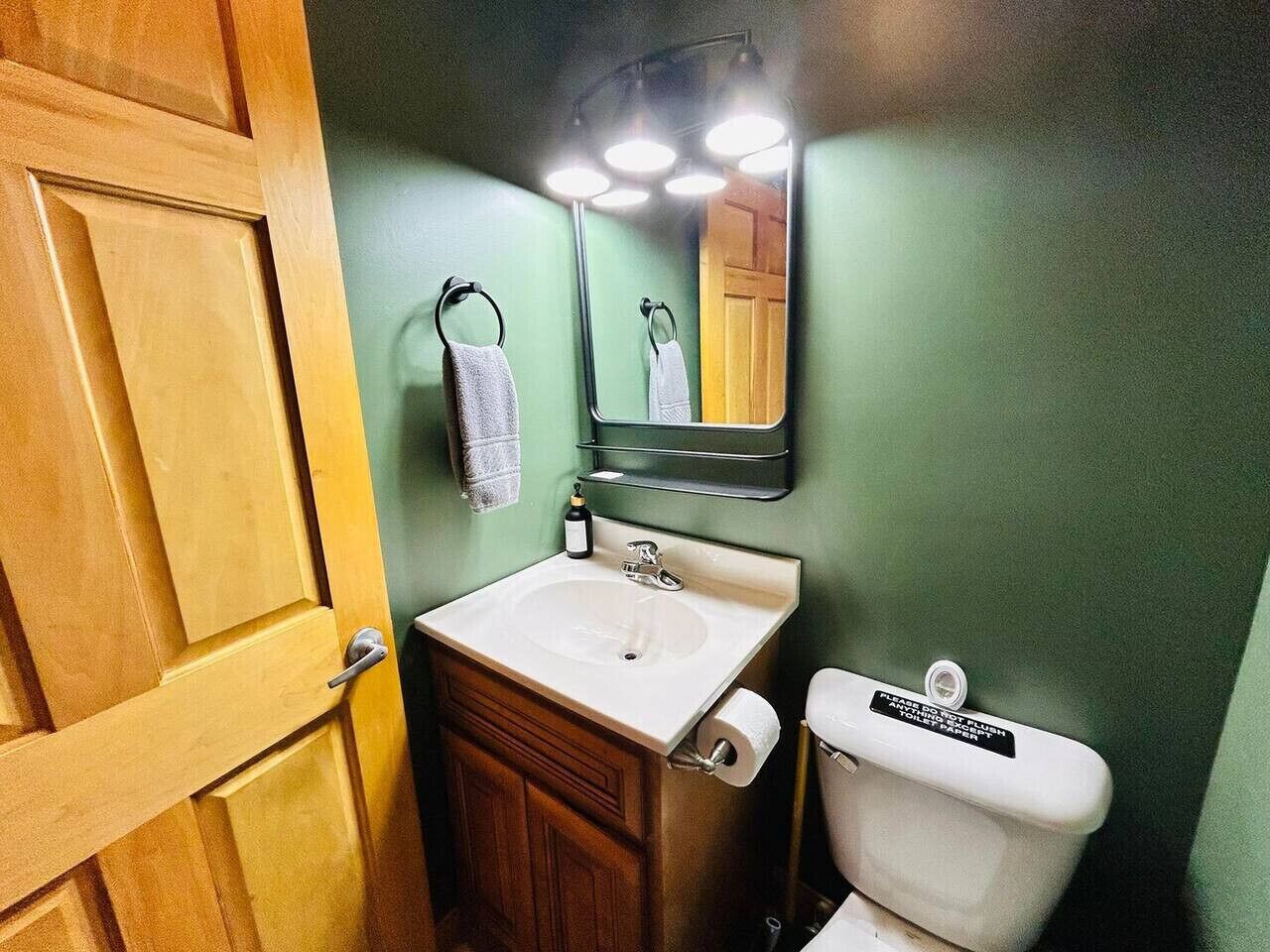 A bathroom with a wooden door, a white sink, a mirror, and a toilet.