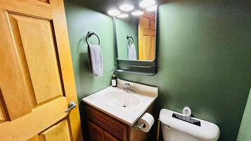 A bathroom with a wooden door, a white sink, a mirror, and a toilet.
