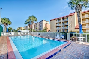 A swimming pool with a tiled edge, surrounded by a white fence, and adjacent to a building with balconies and palm trees. - 202 Atlantis (Fernandina Beach)