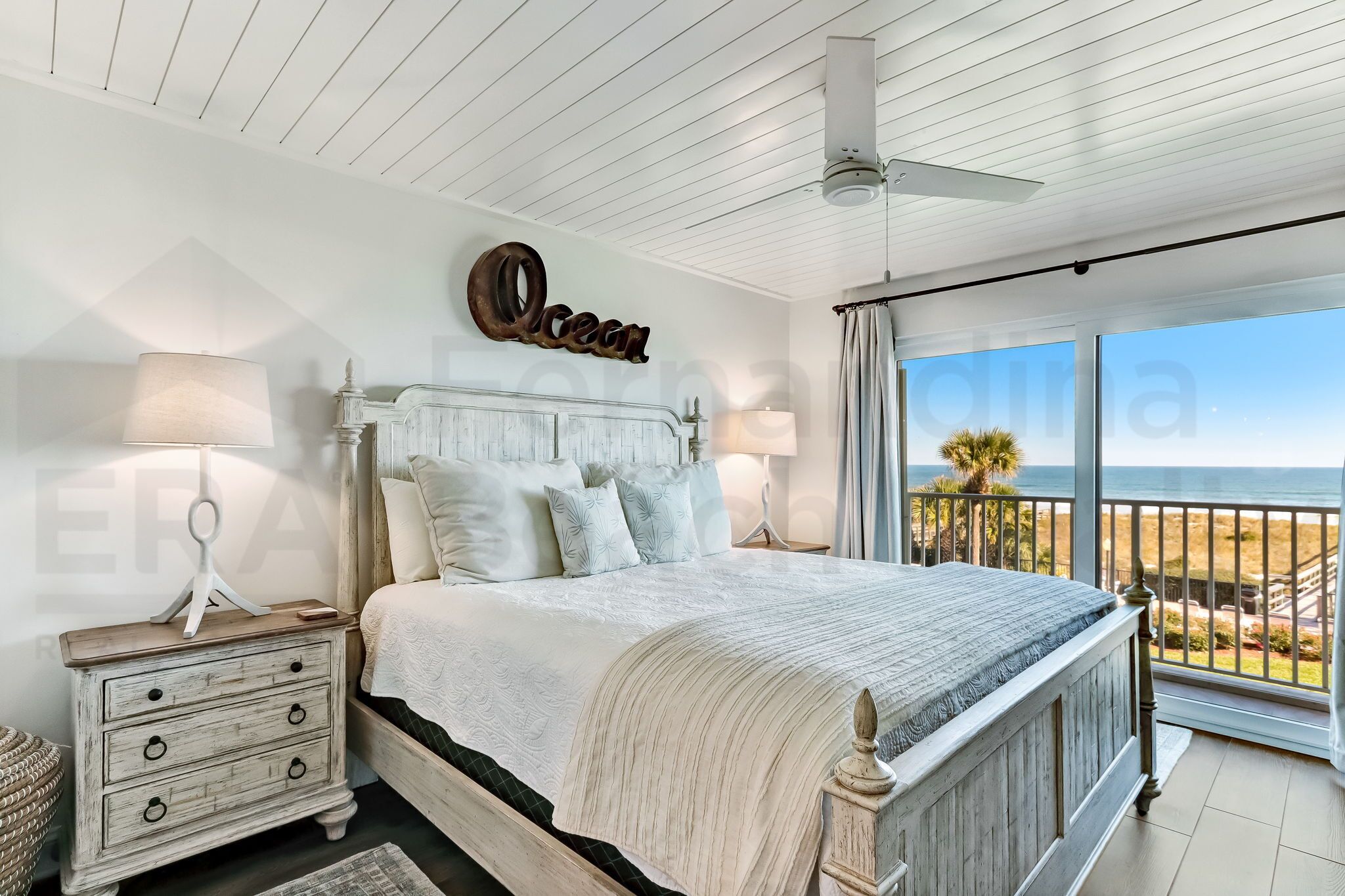 Een slaapkamer met een groot bed, een nachtkastje, een plafondventilator en uitzicht op het strand.