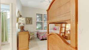 A bedroom with a bunk bed, a bedside table, a lamp, a chair, and a window with blinds.