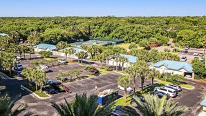 An aerial view of a hotel with a parking lot, surrounded by lush greenery and palm trees.