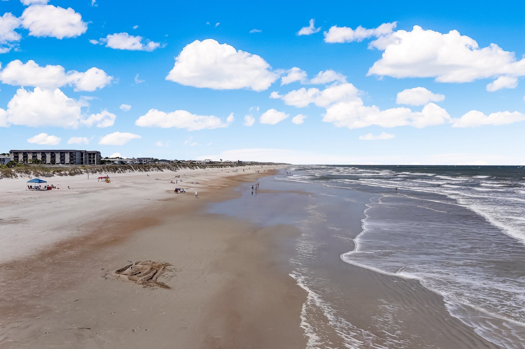 Ein Strand mit einem Gebäude links, sandigem Ufer und Meereswellen.