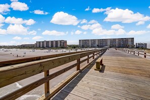 A wooden boardwalk leading to a beach with multiple buildings in the background.