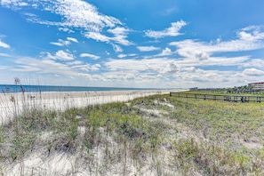 Une plage bordée d’une clôture en bois et de dunes herbeuses.