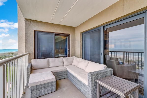 Un balcon avec un canapé en osier, une petite table et une chaise.