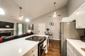 Uma cozinha moderna com ilha central, armários brancos, geladeira e área de jantar com uma mesa e cadeiras.