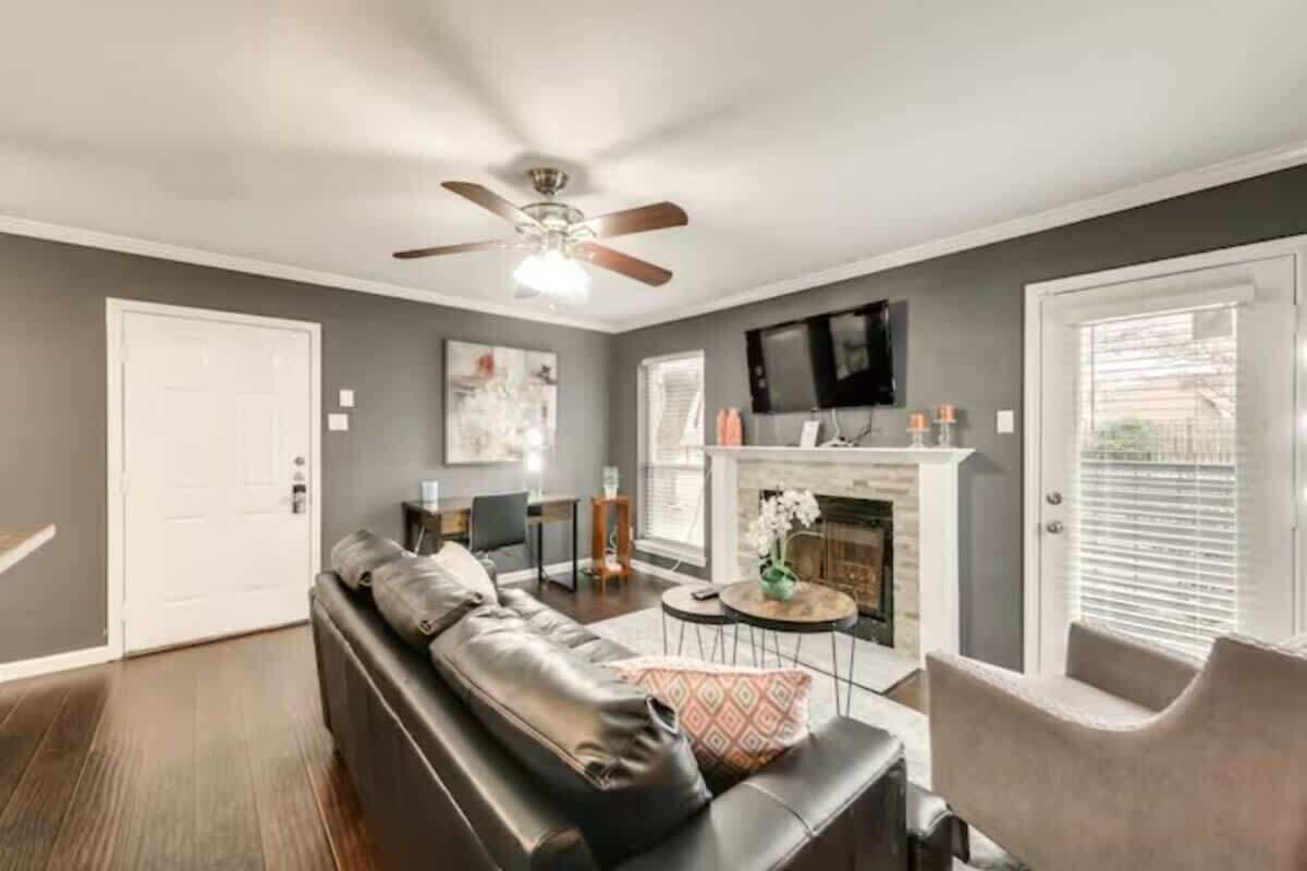 A living room with a leather sofa, a fireplace, a ceiling fan, and a TV mounted on the wall.