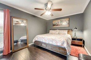 Quarto com cama, ventoinha no teto, espelho grande, mesa de cabeceira e janela com cortinas.