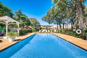 Piscina retangular com deck de madeira, rodeada por árvores e um gazebo.