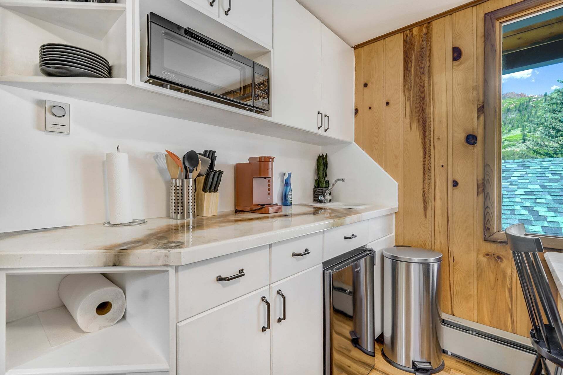 A kitchen with white cabinets, a stainless steel microwave, a coffee maker, and a trash can.