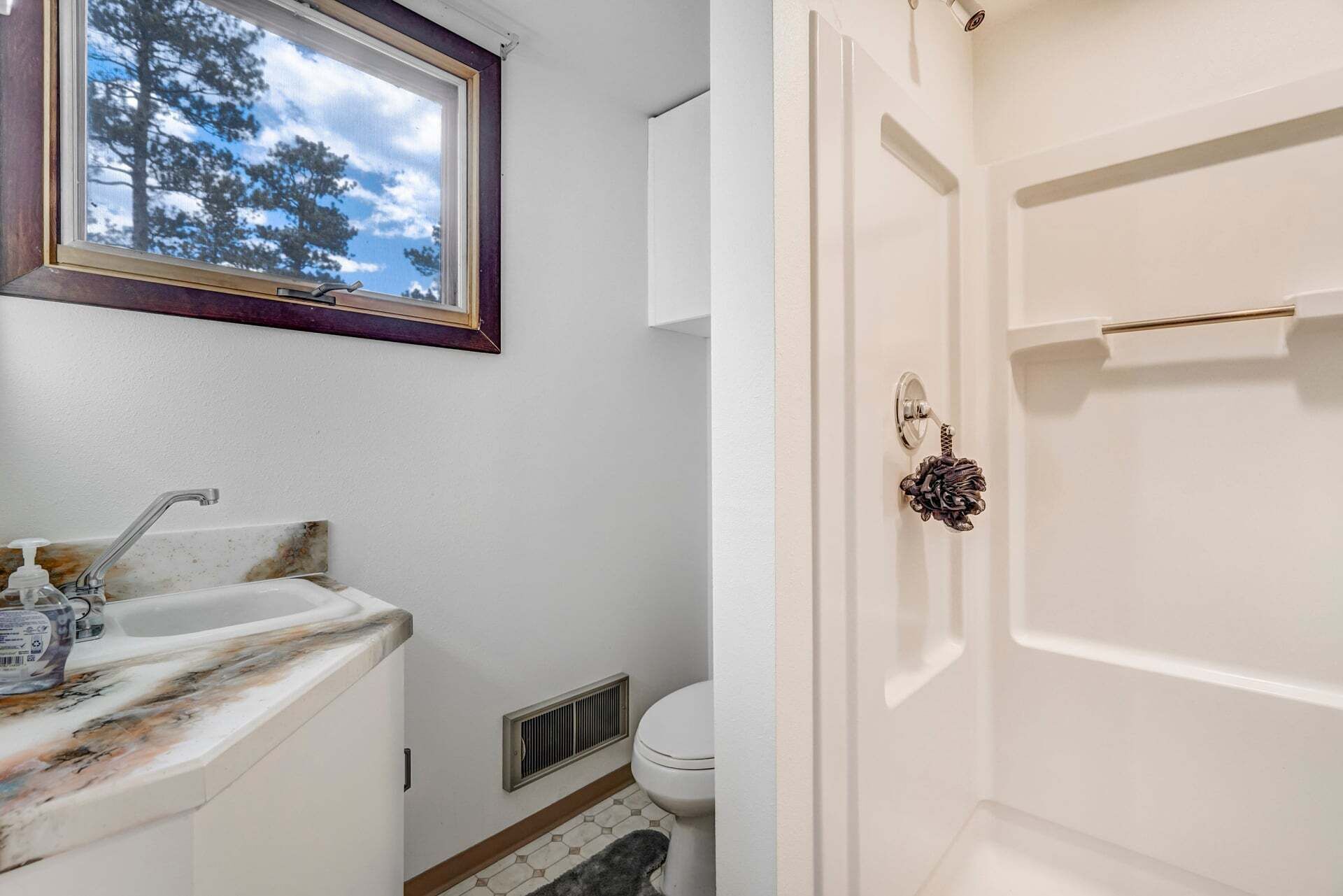 A bathroom with a window, a sink, a toilet, and a shower door.