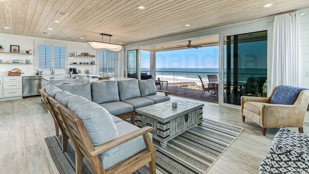A modern kitchen with a large island, a dining area with a view of the beach, and a living room with a sofa and coffee table. - 226 South Fletcher 3rd Floor (Fernandina Beach)