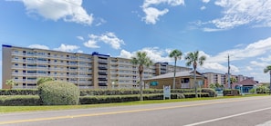 A multi-story hotel with balconies, a small adjacent building, and palm trees.