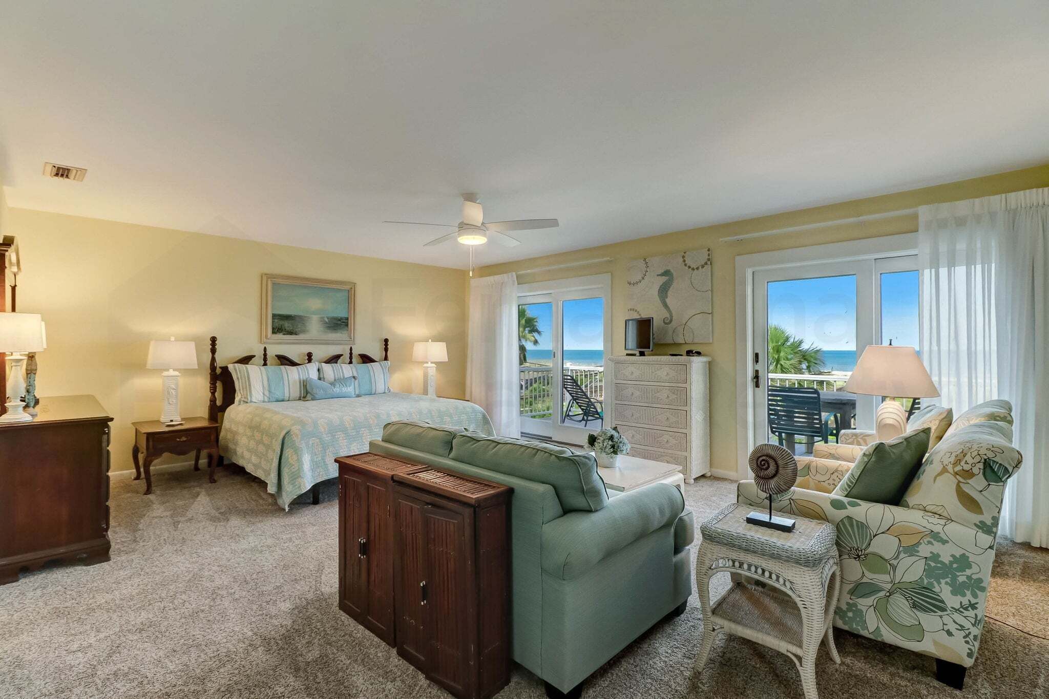 A bedroom with a bed, a sofa, a dresser, a ceiling fan, and a view of the ocean.